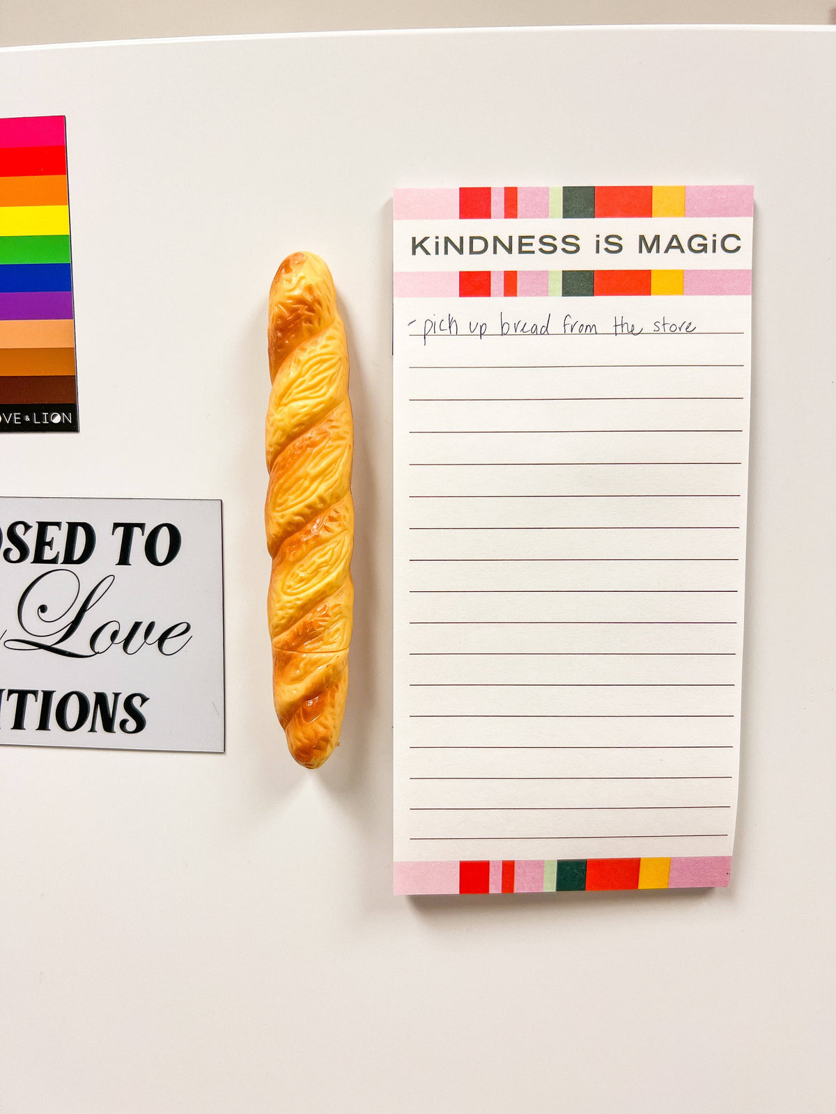Notepad with 'Kindness is Magic' text and a baguette pen on, all magnetized to a fridge.