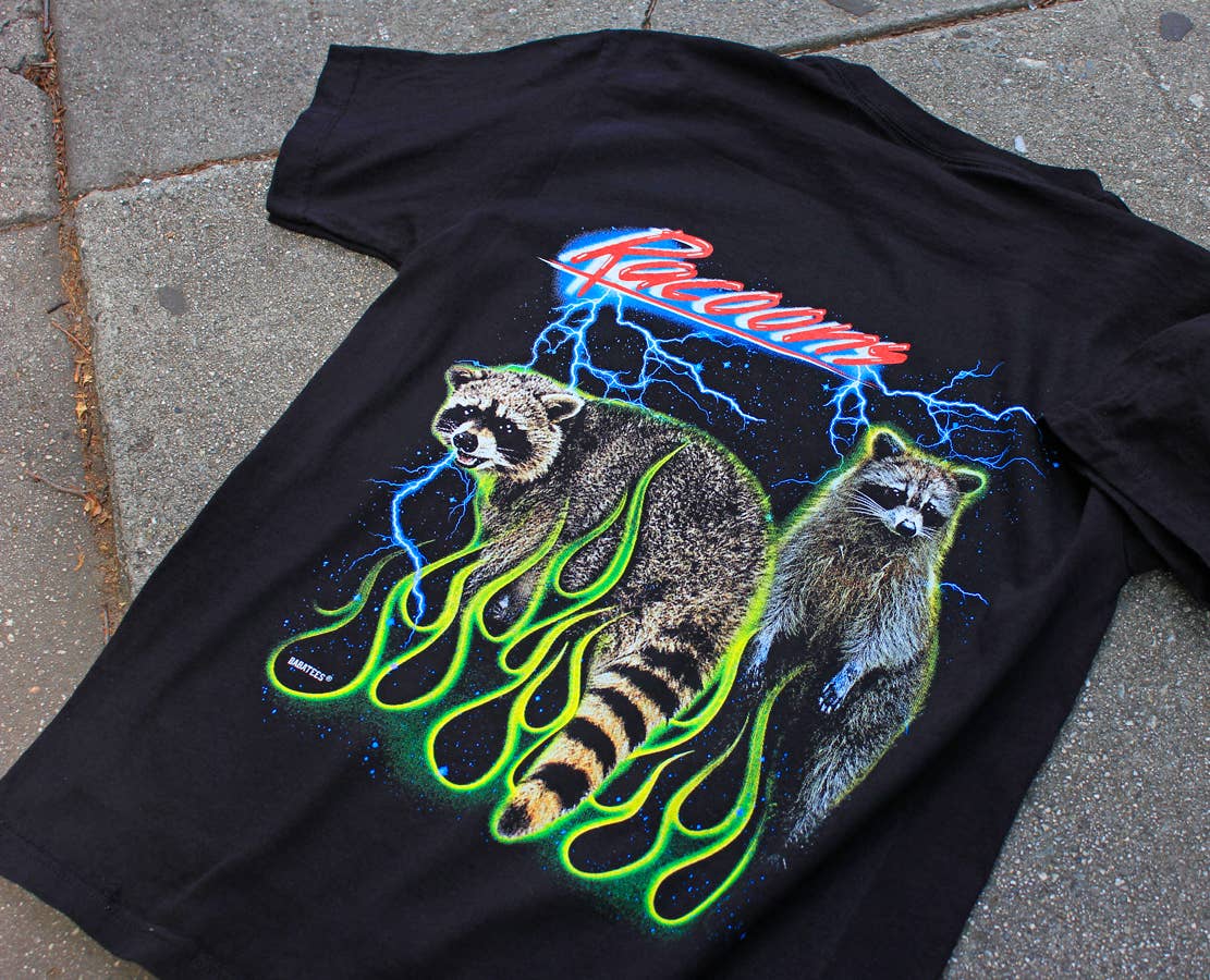 Black t-shirt with raccoon graphic and 'Racoons' text on a concrete surface