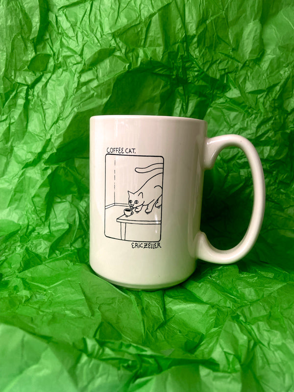 A beige ceramic coffee mug with a black line art illustration of a cat sniffing coffee, text Coffee Cat' written at the top, set against a crumpled green paper background.